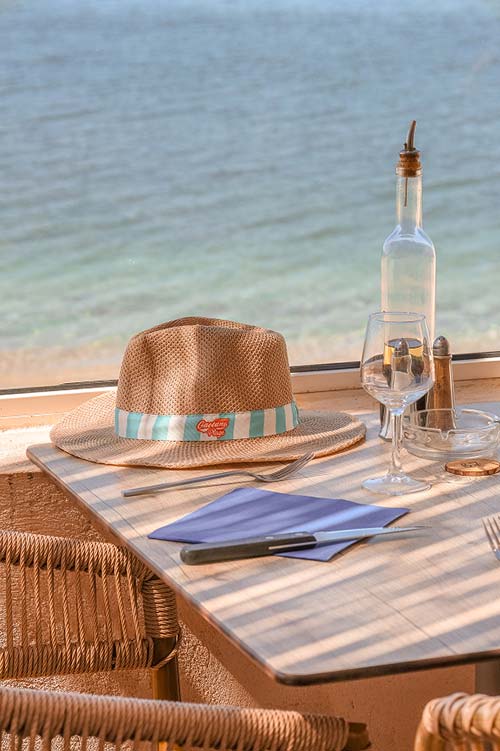 Gaetano Plage — Table vue mer sur la plage de l'Almanarre à Hyères Table dressée avec chapeau de paille Gaetano face à la mer turquoise au restaurant Gaetano Plage l'Almanarre à Hyères